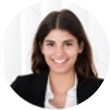 Lächelnde Frau mit dunklem Haar, schwarzem Blazer und weißem Hemd, Vertreterin einer Webdesign-Agentur in Buchholz in der Nordheide, sitzt vor hellem Hintergrund.
