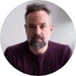 Ein Mann mit kurzen dunklen Haaren und Bart sowie einem dunklen Hemd sitzt im Innenbereich und blickt in die Kamera – ideal für die Darstellung einer Webdesign-Agentur aus Buchholz in der Nordheide.